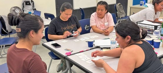 Parents and children working together on a hands-on math card activity at a classroom table.