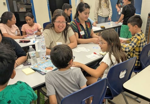 Parents and children collaborating on a hands-on math activity at a classroom table.
